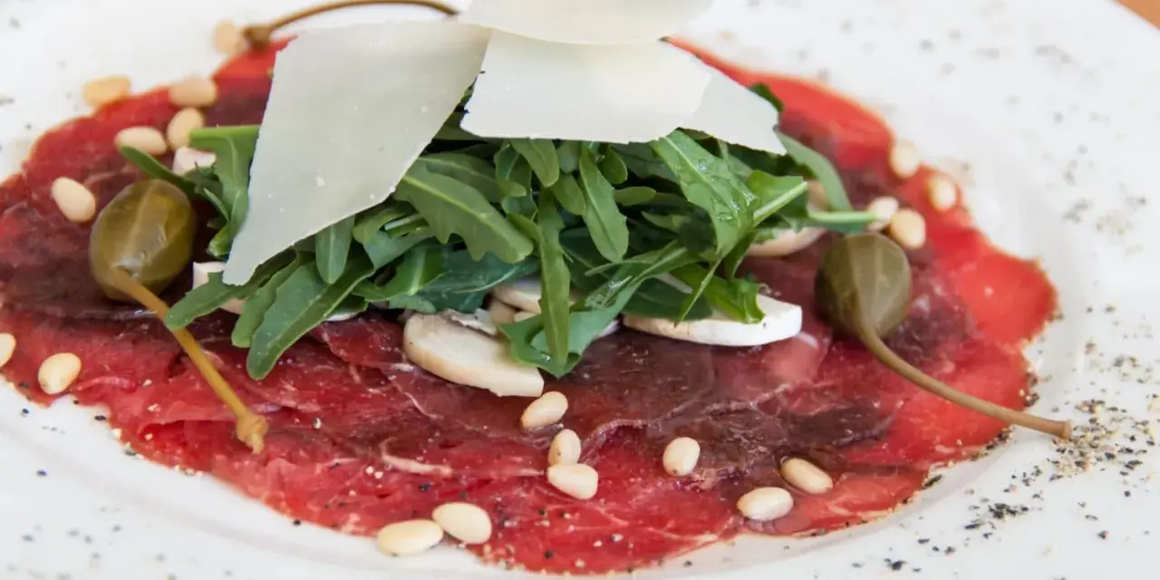Delicato carpaccio di manzo con rucola, scaglie di parmigiano, pinoli, capperi e funghi.