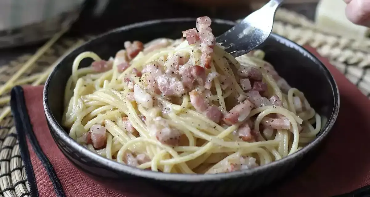 Un tenedor recoge espaguetis cremosos con trozos de bacon crujiente, creando un delicioso plato de pasta con bacon.