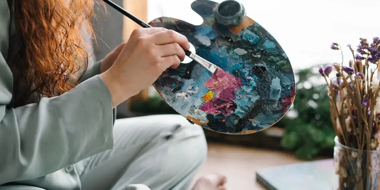 Une artiste aux cheveux roux mélange des couleurs vives sur sa palette, prête à peindre. Apprenez comment utiliser la peinture acrylique pour créer de telles œuvres.