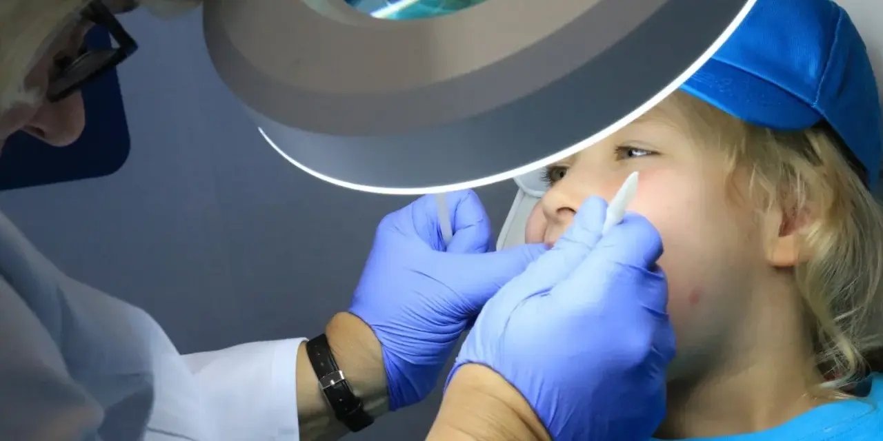 Dentysta w rękawiczkach bada usta dziecka pod lampą powiększającą.