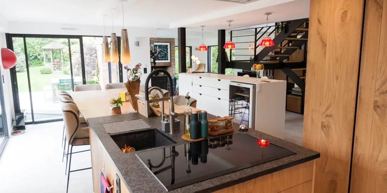 Îlot de cuisine moderne avec plan de travail en granit, évier noir et plaque à induction. La **rénovation cuisine bois massif** se révèle dans les placards et l'îlot central.