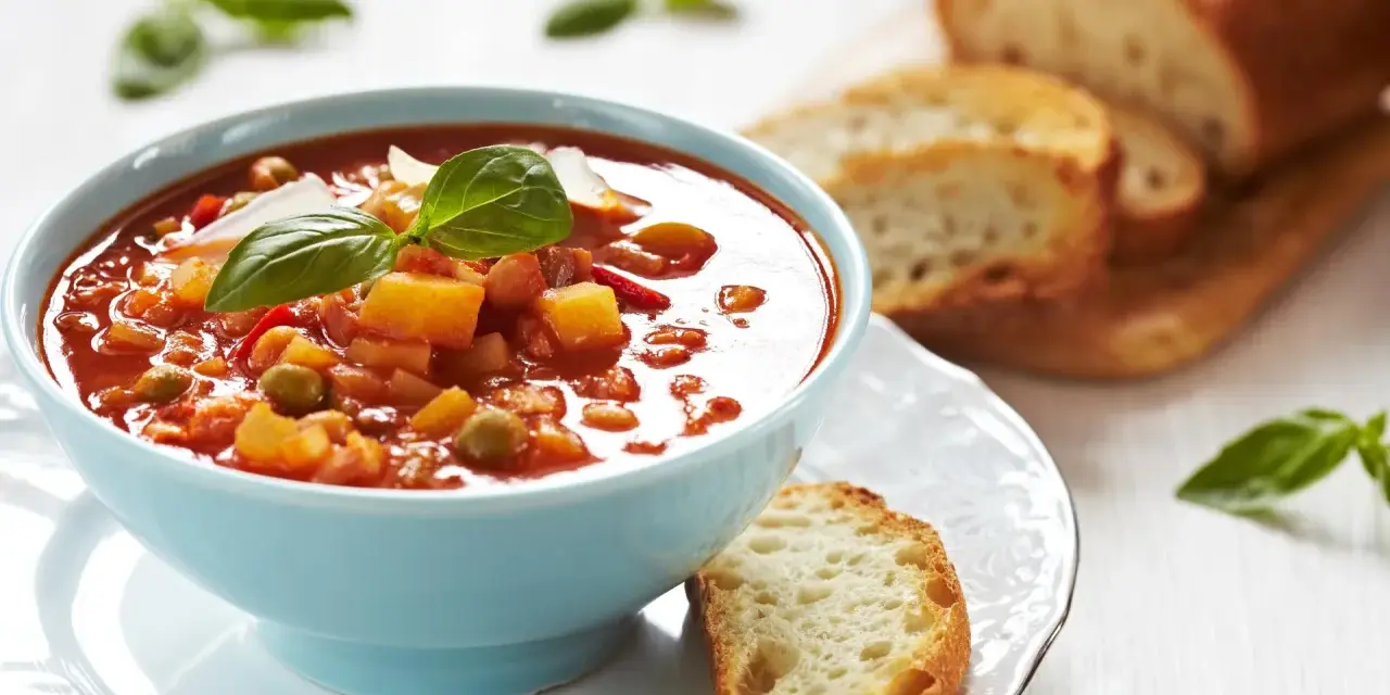 Zupa jarzynowa a minestrone w niebieskiej miseczce, udekorowana bazylią, podana z chrupiącym pieczywem.