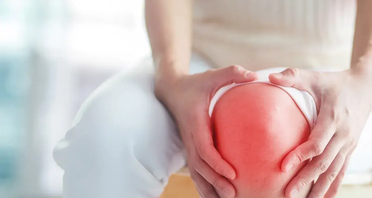 Hände umfassen ein schmerzendes Knie, das rot aufleuchtet, ein Zeichen für Arthrose im Knie.