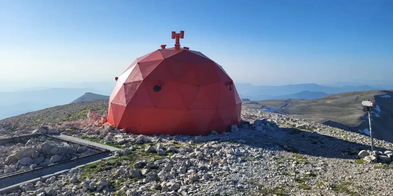 Struttura rossa a cupola su un terreno roccioso, con vista panoramica sulle montagne del Monte Amaro.