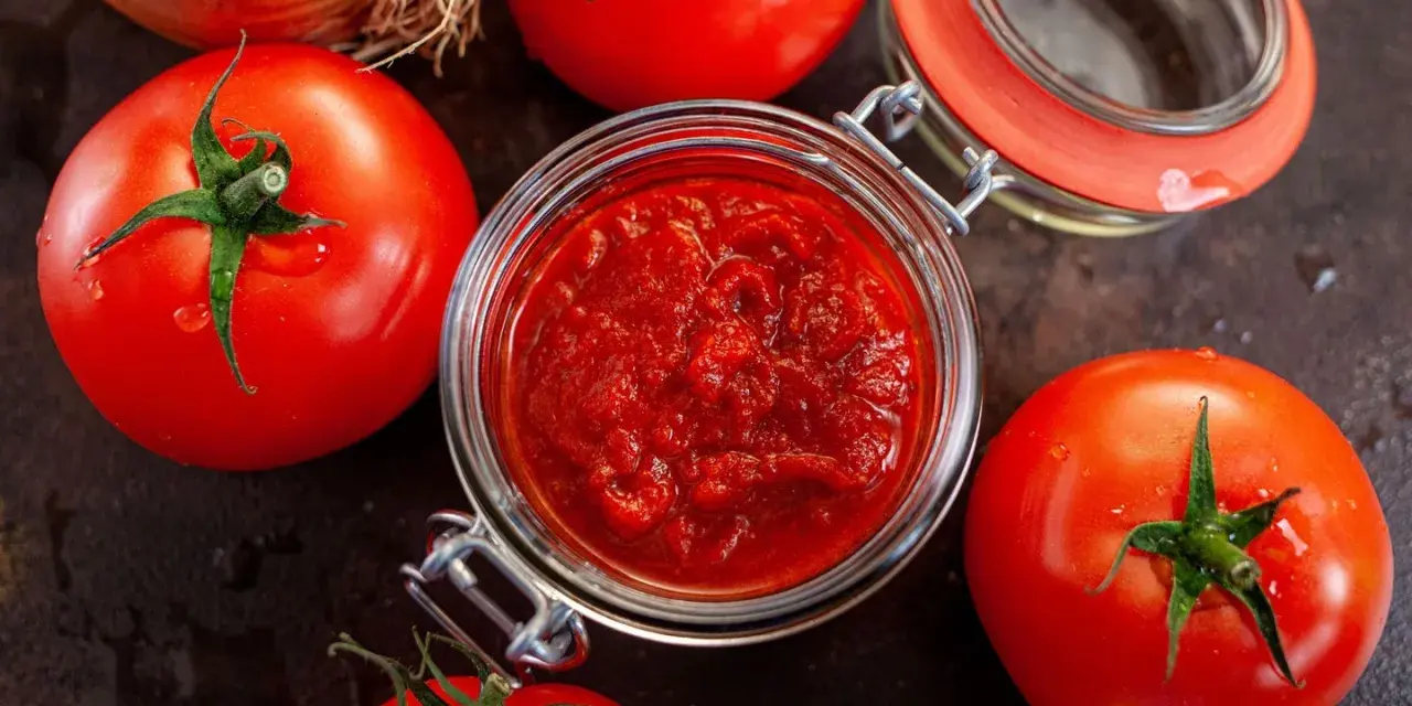 Frische Tomaten um ein Glas mit selbstgemachtem Tomatenmark. Perfekt für Saucen und mehr!