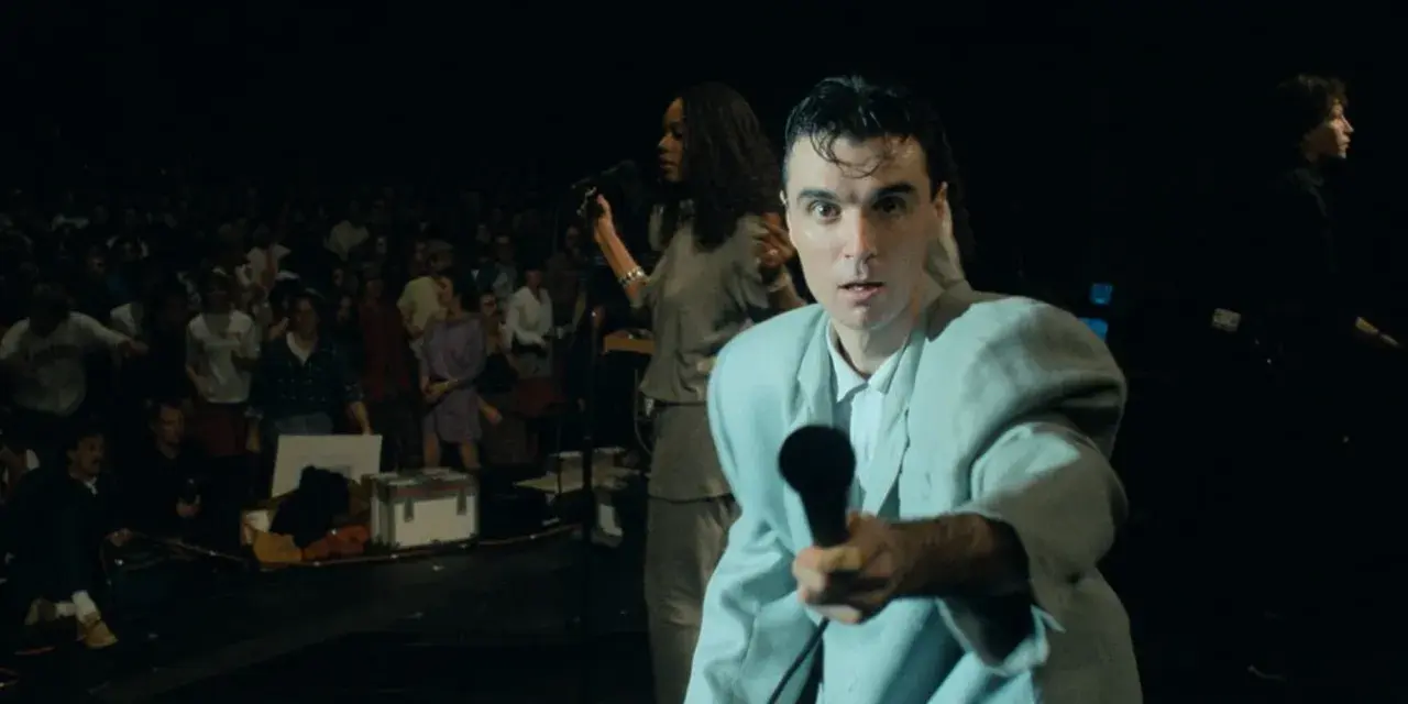 David Byrne z The Cult - Be Free, śpiewa do mikrofonu na tle tłumu.
