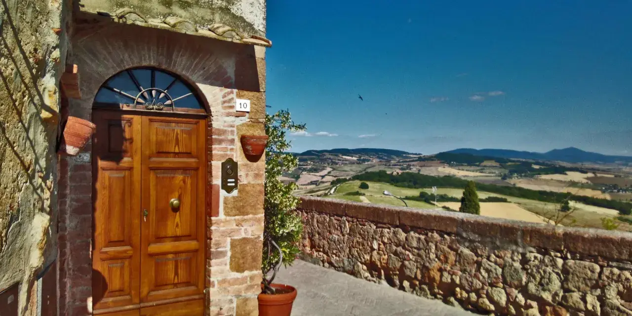 Un portone in legno in un borgo toscano, con vista panoramica sulle colline. Perfetto per un tour in moto tra i borghi più belli della Toscana.