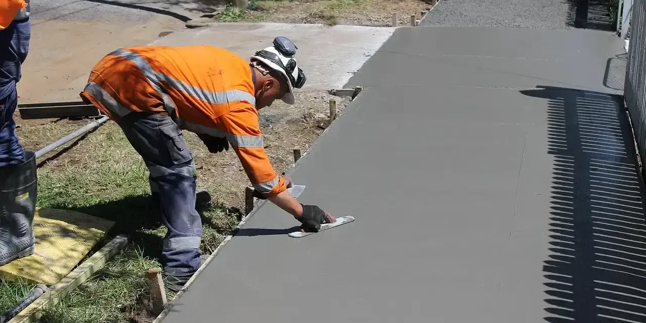 Robotnik w pomarańczowej kamizelce wygładza świeży beton. Zastanawiasz się, ile kosztuje kubik betonu na taki podjazd?
