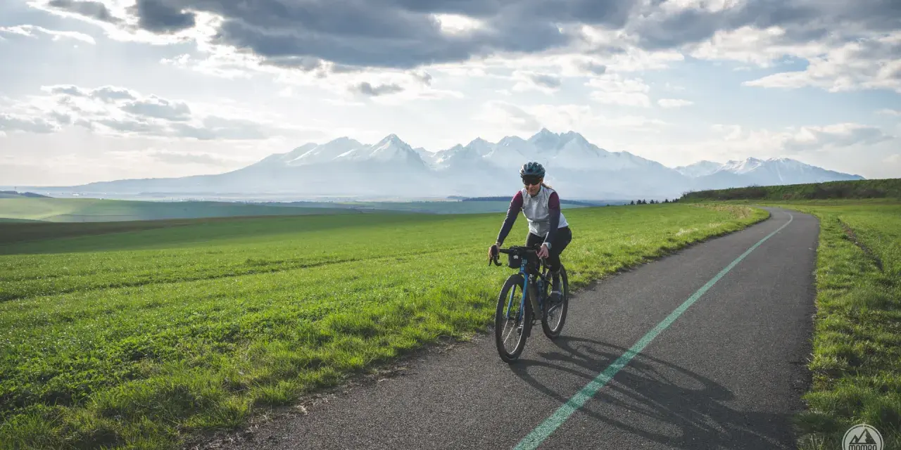 Kobieta na rowerze pokonuje malowniczą trasę z widokiem na ośnieżone Tatry. To wyzwanie: rowerem dookoła Tatr w jeden dzień!