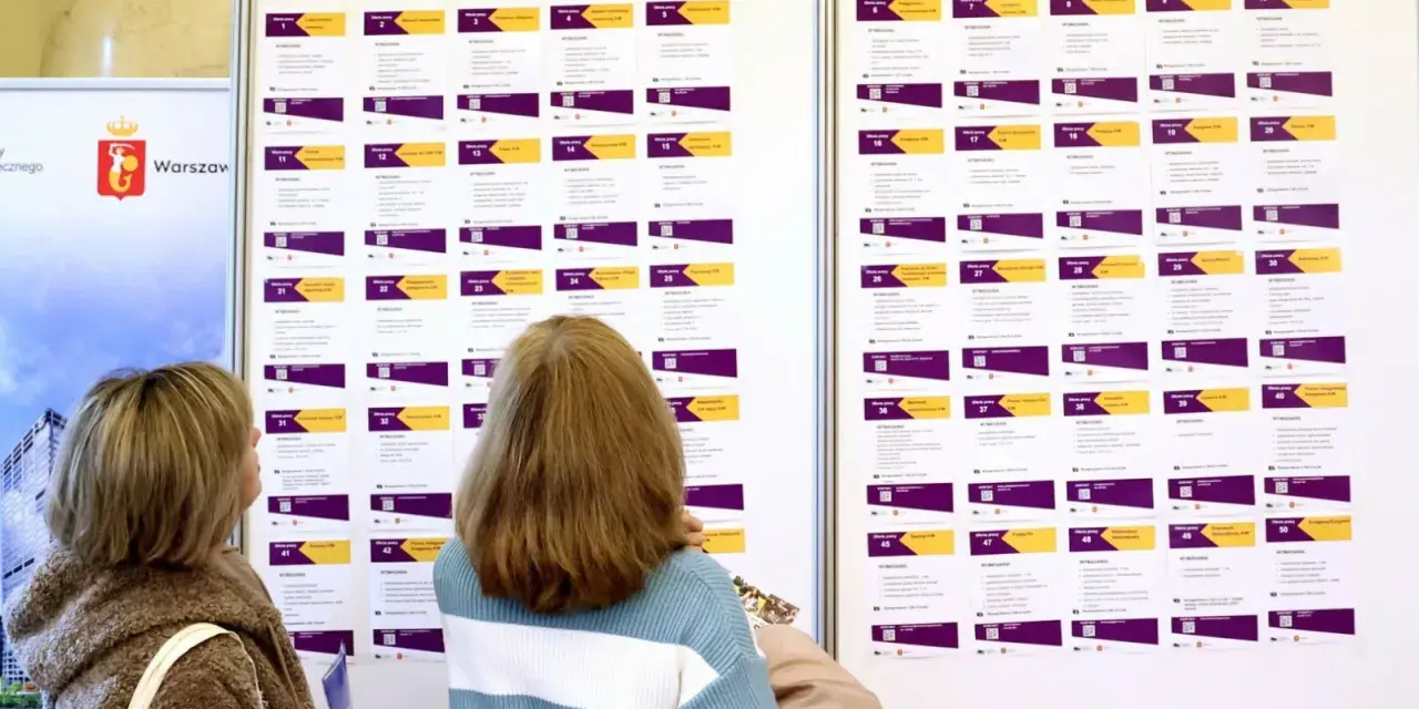 Dwie kobiety przeglądają tablicę z ofertami pracy, szukając rozwiązań problemu bezrobocia w Polsce.
