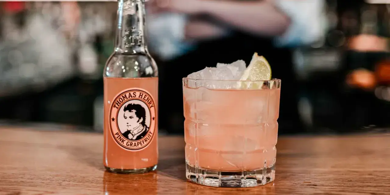 En rosa tequila drink med is och lime, bredvid en flaska Thomas Henry Pink Grapefruit.