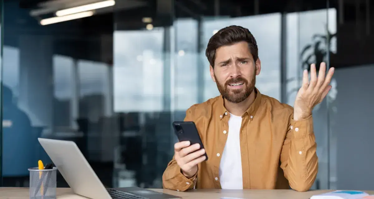 Zdezorientowany mężczyzna trzyma telefon, jakby właśnie dowiedział się o problemach z cesją.