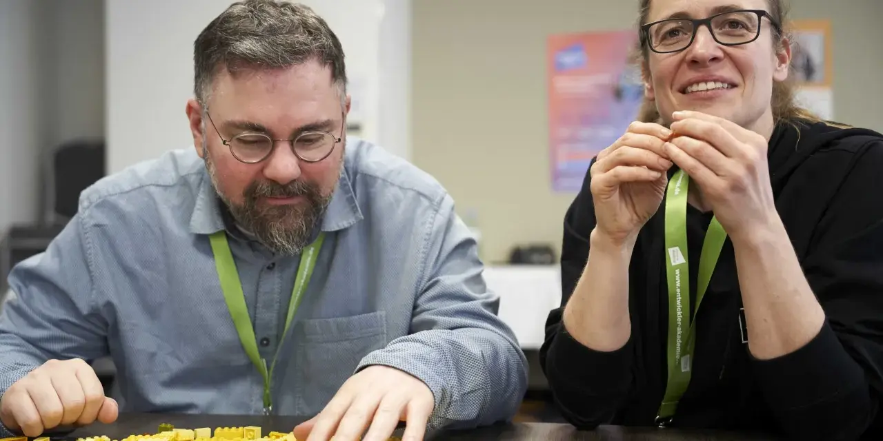 Zwei Personen bauen mit bunten Legosteinen, während sie an einem software architecture summit teilnehmen.