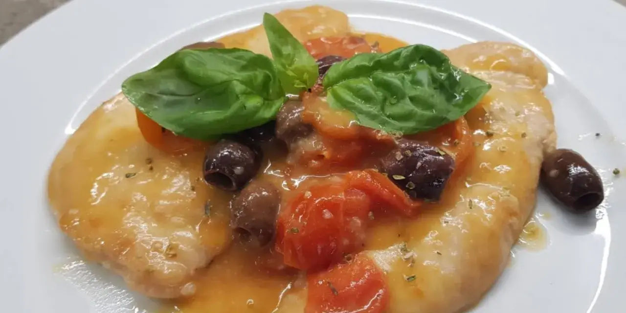 Delizioso pollo alla mediterranea con pomodorini, olive nere e basilico fresco su un piatto bianco.