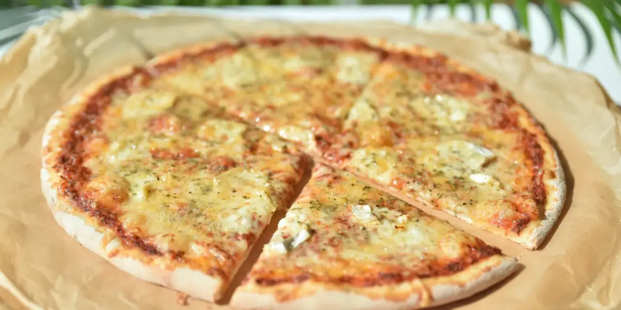 Pizza 4 sery z roztopionym serem i ziołami na papierze do pieczenia.