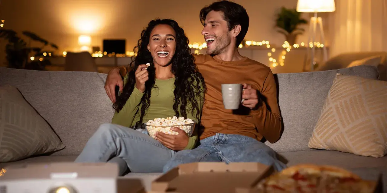 Ein lachendes Paar genießt einen gemütlichen Filmabend mit Popcorn und Pizza. Perfekte filmabend snacks für einen entspannten Abend.