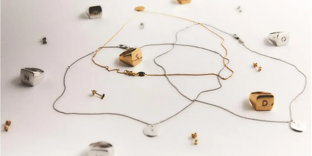 Joyas con letras, como limpiar la plata para que brillen. Anillos y collares dorados y plateados sobre fondo blanco.