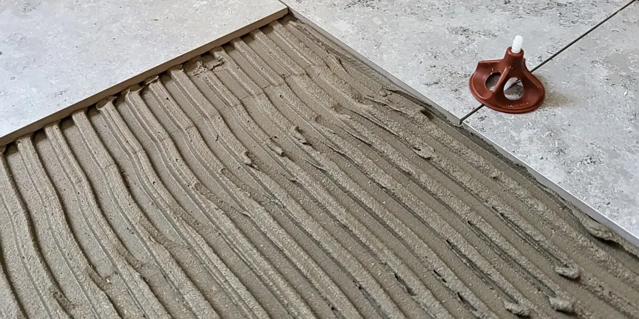 Läggning av klinker på betonggolv med fix. En del av golvet är täckt med fix, redo för nästa platta.