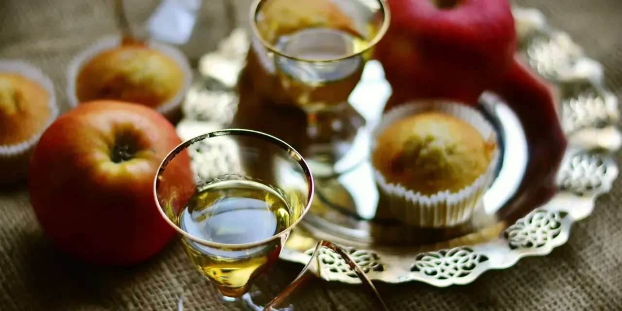 Zwei Gläser mit goldenem Schnaps, Äpfel und Muffins auf einem Silbertablett. Perfekt für den Genuss von selbstgemachtem Kartoffelschnaps.