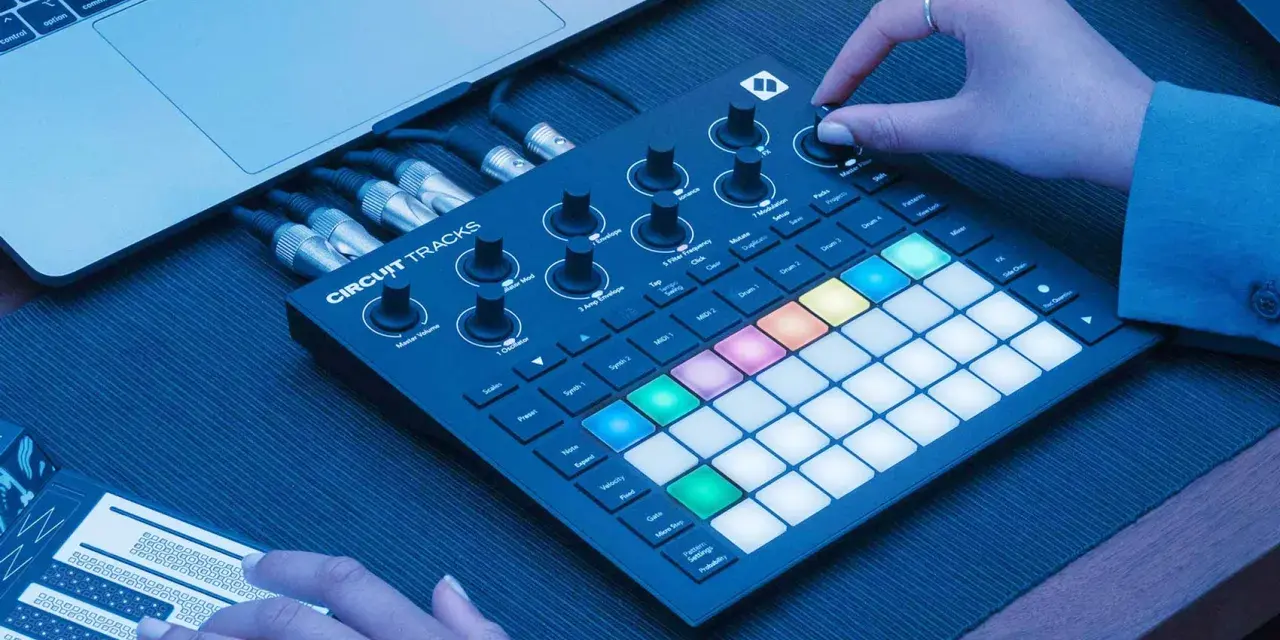 Ręce tworzą muzykę na Novation Circuit Rhythm, z podłączonym laptopem i kablami.