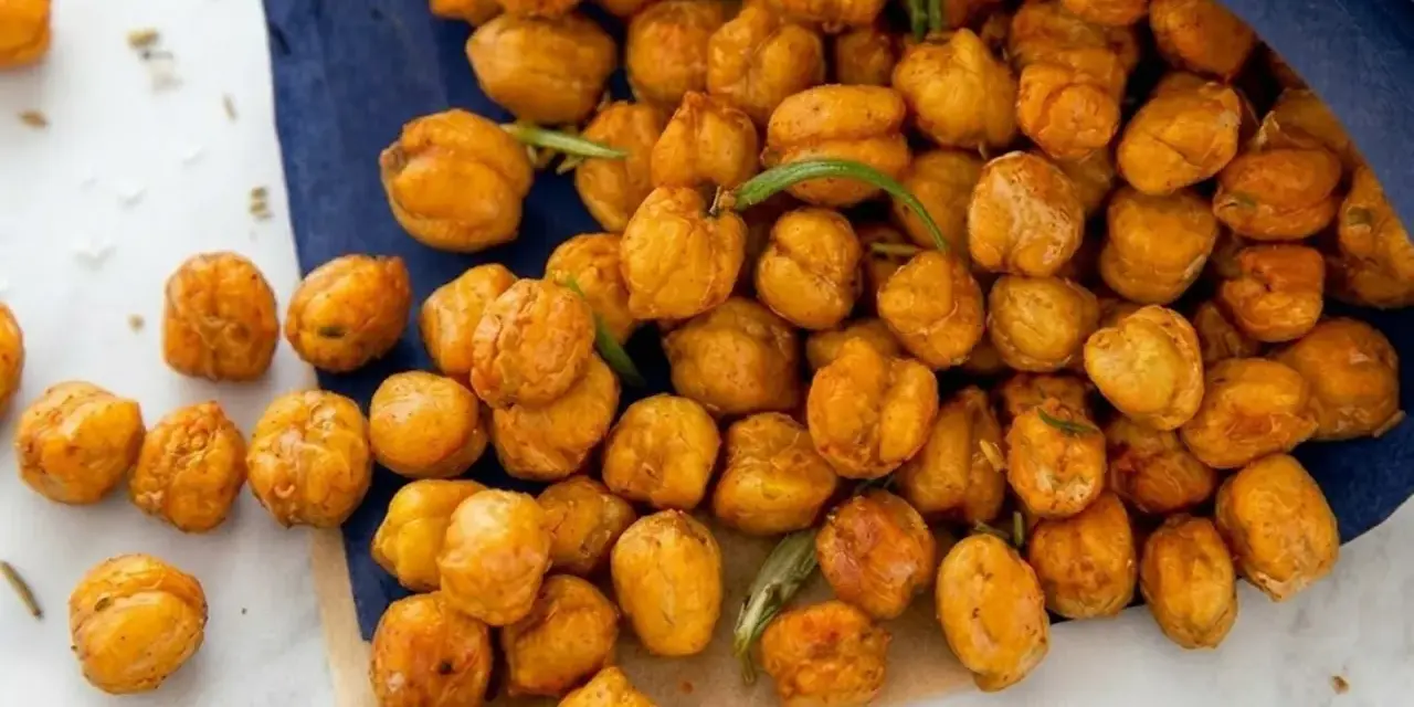 Un sacchetto blu rovesciato rivela una montagna di ceci croccanti al forno, dorati e invitanti, con qualche rametto di rosmarino sparso tra loro.