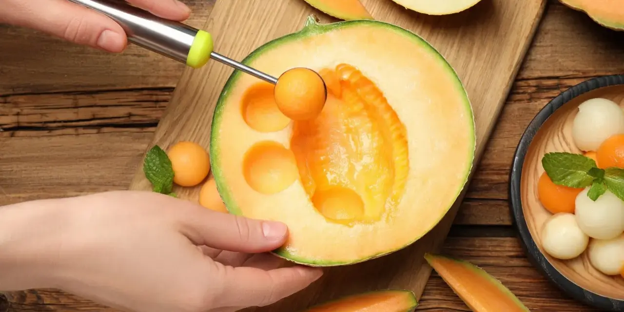 Ręka z gałkownicą wydobywa kulki z melona, ukazując jego soczyste wnętrze. Melon właściwości odżywcze czynią go idealnym na letnie orzeźwienie.