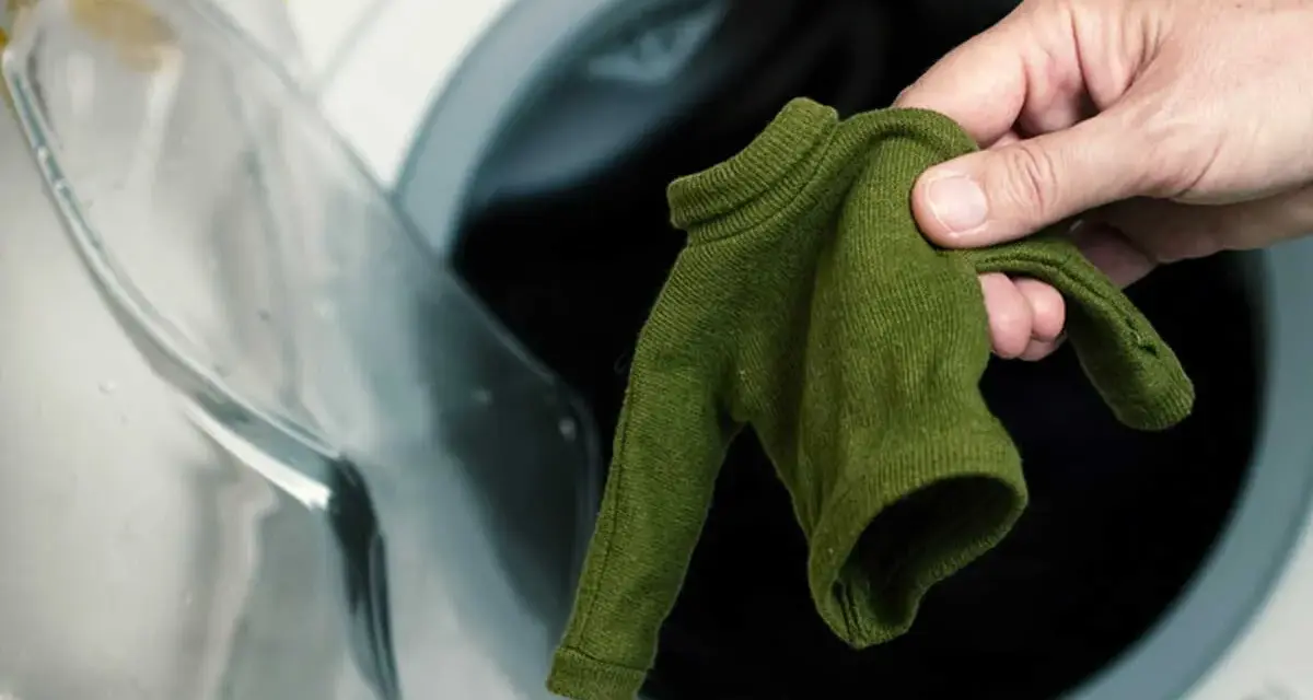 Main verte, petite, tenue dans une main, devant une machine à laver ouverte. Le coton rétrécit il au lavage ?