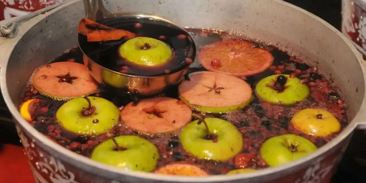Gorące wino z jabłek bez drożdży, z dodatkiem plasterków jabłek, pomarańczy i cynamonu, gotujące się w dużym garnku.