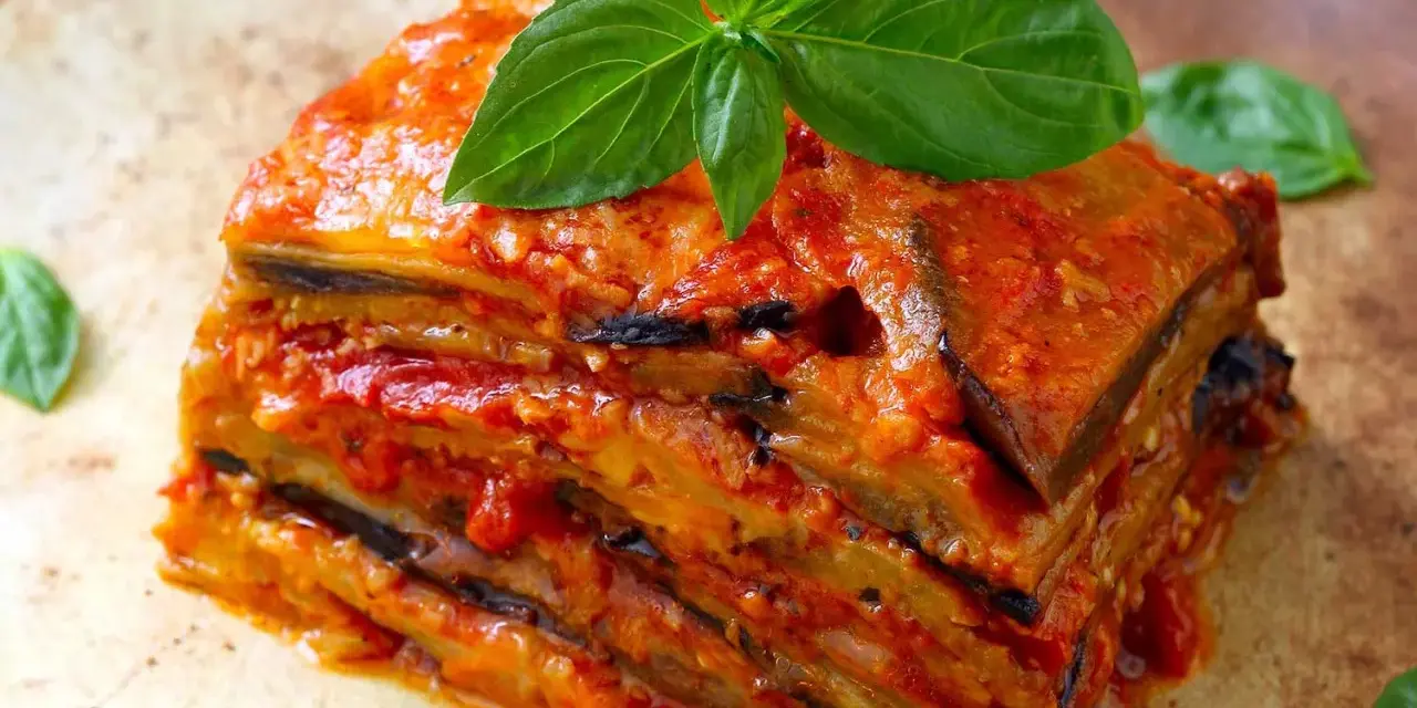 Una fetta di parmigiana di melanzane, stratificata e succulenta, guarnita con basilico fresco.