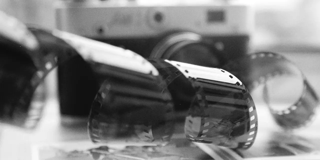 Analogowa fotografia: zwoje kliszy filmowej przed aparatem, na tle książki z napisem "DANIEL KONI".
