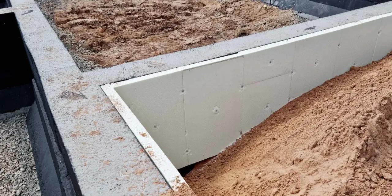 Fundament pod altanę w budowie: betonowe ławy, izolacja ze styropianu i nasypy ziemi. Słupki fundamentowe pod altanę czekają na montaż.