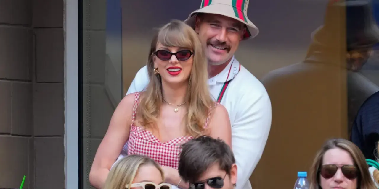 Travis Kelce e Taylor Swift sorridono, lei con un vestito a quadri rossi, lui con un cappello Gucci.