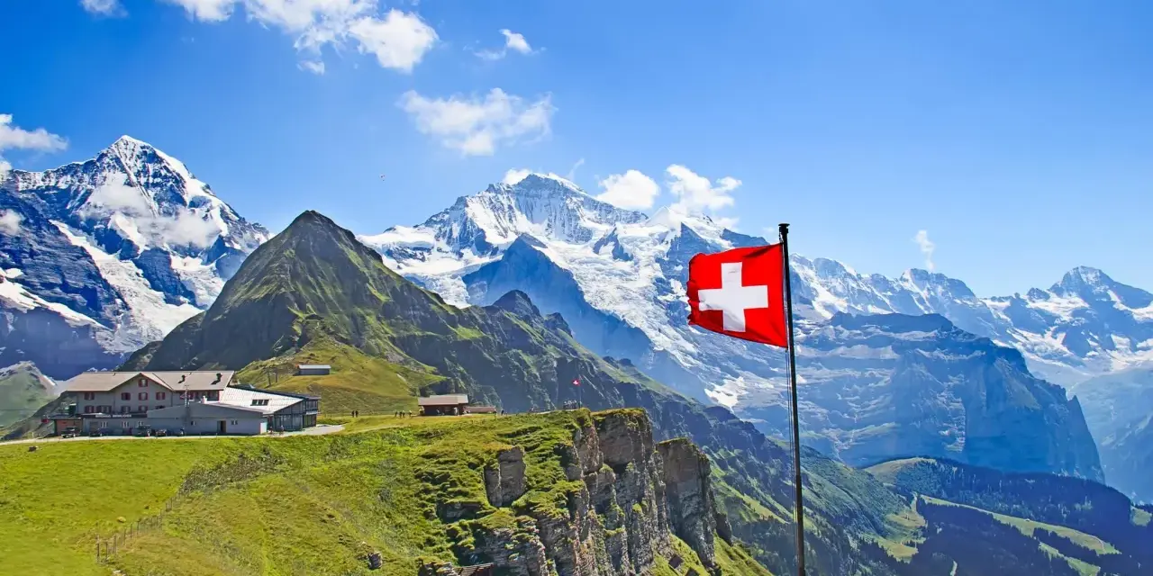A Swiss flag flies proudly against a backdrop of majestic snow-capped mountains and lush green slopes, showcasing the beautiful places of nature in Switzerland.
