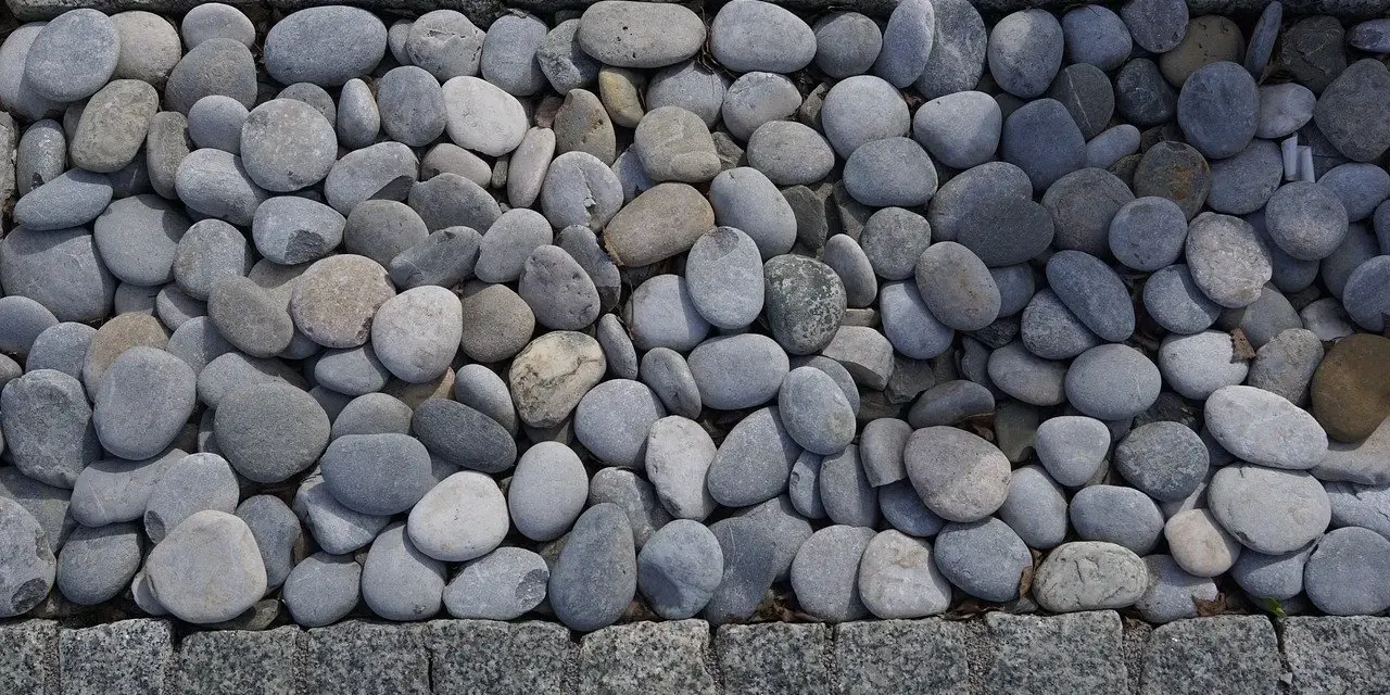 Gładkie, szare kamienie tworzą naturalną dekorację w ogrodzie, otoczone granitową kostką.