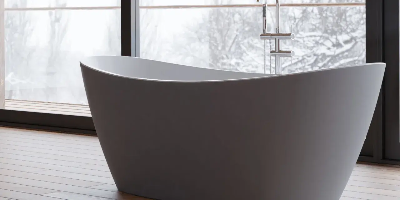 Baignoire îlot moderne, avec robinetterie chromée, devant une grande fenêtre donnant sur un paysage hivernal. Les inconvénients de ce type de baignoire sont son encombrement et la nécessité d'une installation spécifique.