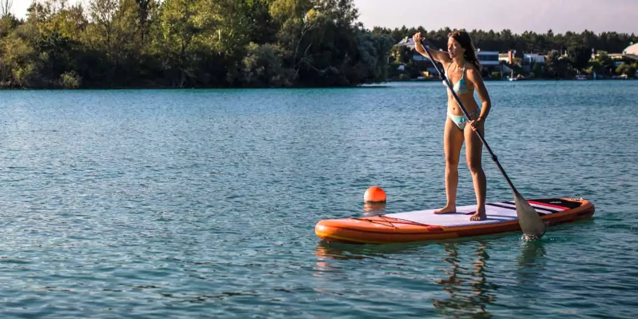 Frau genießt das sub fahren auf einem ruhigen See, umgeben von grünen Bäumen und Häusern.