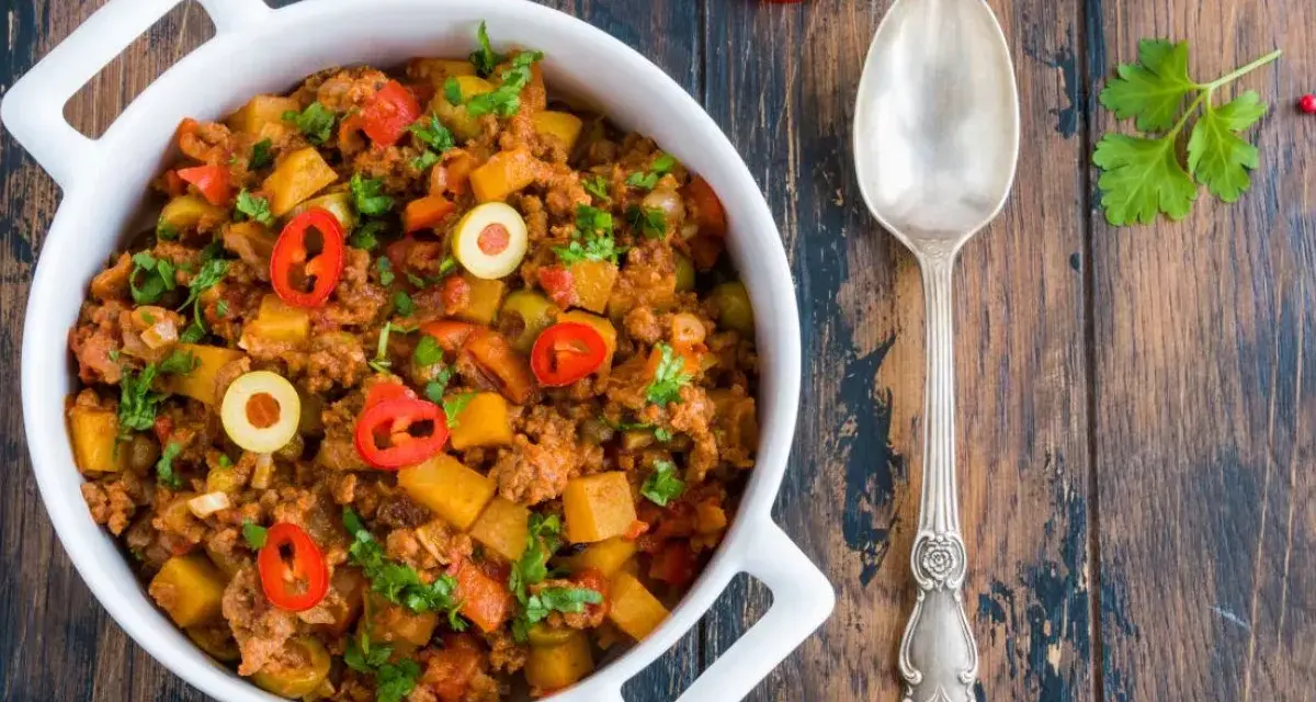 Pyszne danie z mielonego mięsa wołowego z ziemniakami, oliwkami i papryczką chili, posypane natką pietruszki.