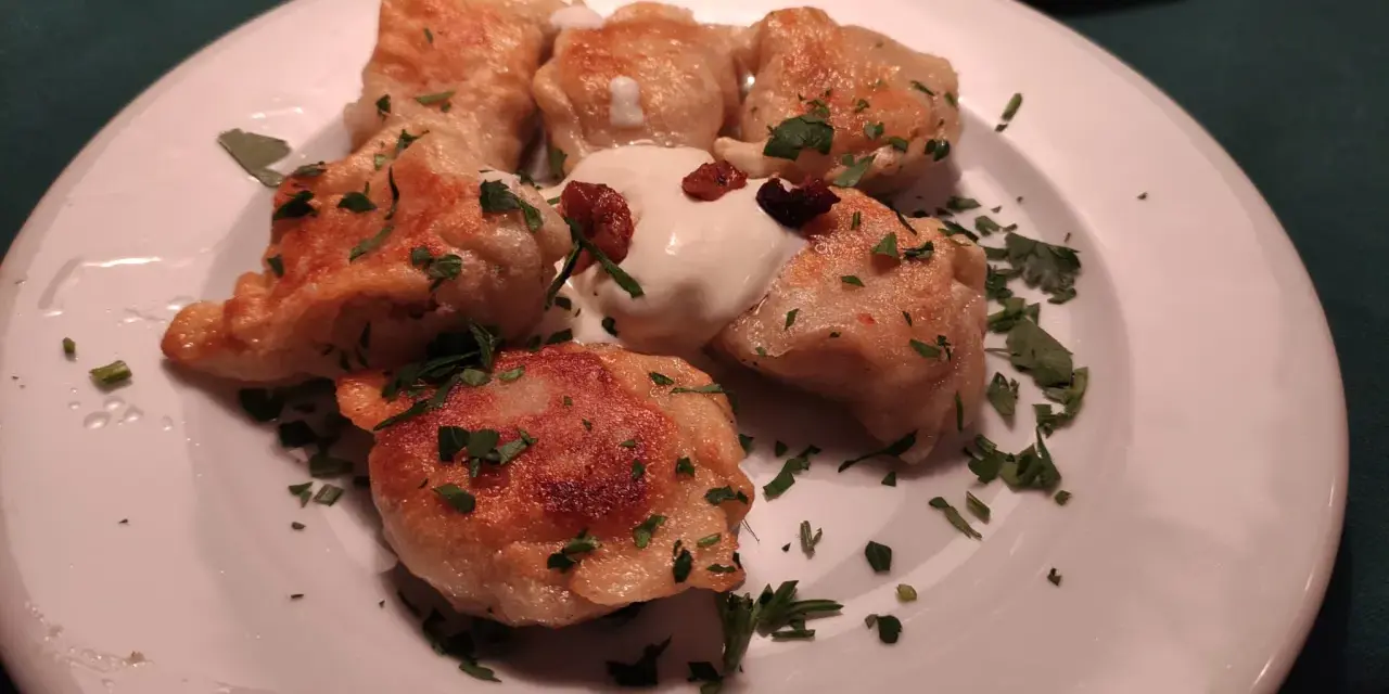 Pierogi, un piatto tipico polacco, serviti su un piatto bianco con panna acida e prezzemolo tritato.
