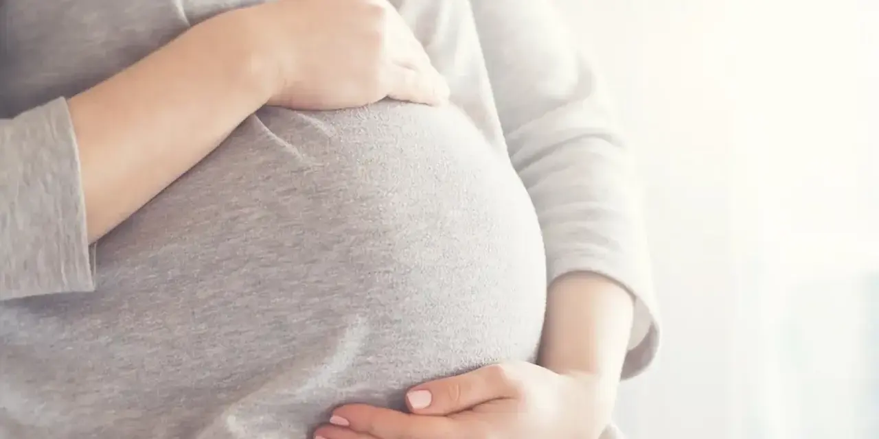 Brzuszek w 6 miesiącu ciąży, delikatnie otulony dłońmi.