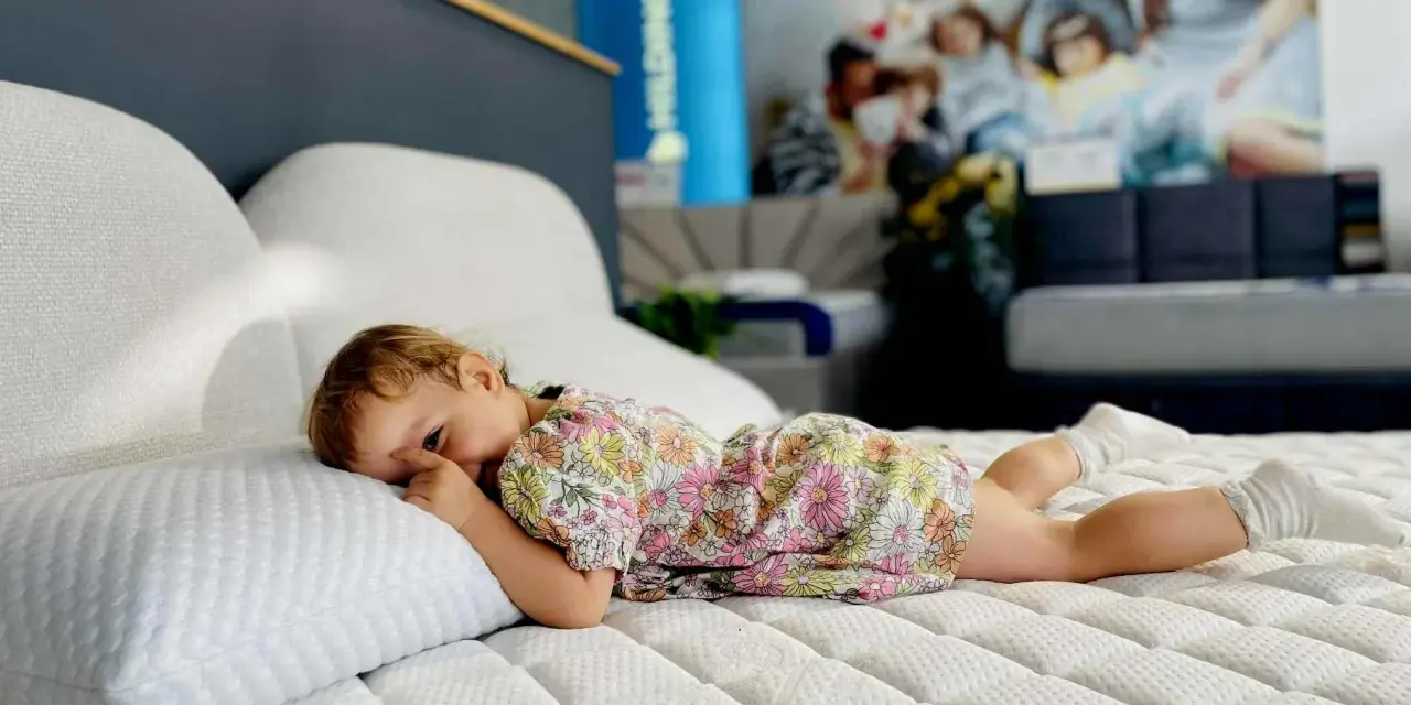 Małe dziecko w kwiecistej sukience leży na materacu. Czy lateks jest szkodliwy? Ten materac wygląda na bardzo wygodny.
