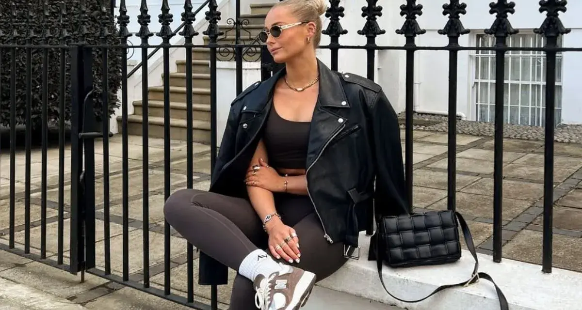 Kobieta w skórzanej kurtce i legginsach, uosobienie stylu athleisure, siedzi na murku przed kamienicą.