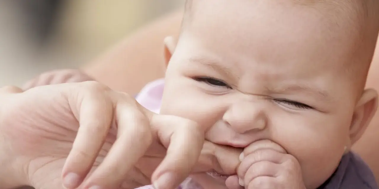 Ein süßes Baby mit einem lustigen Gesichtsausdruck, das gerade versucht, den Finger einer erwachsenen Person zu beißen.