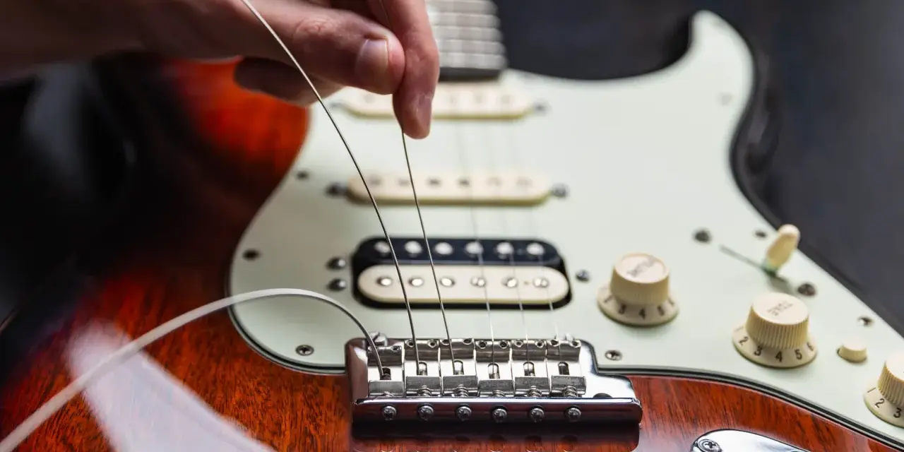Dłoń naciąga nowe struny w gitarze elektrycznej, przygotowując ją do gry.