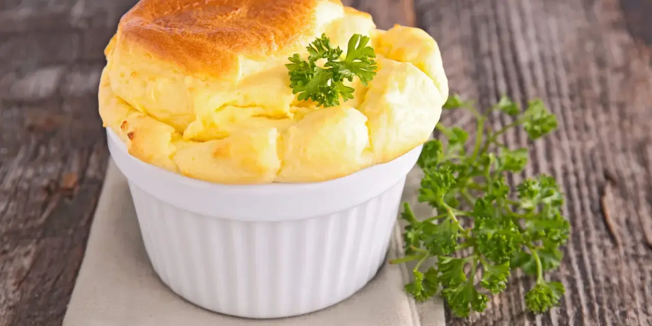 Un soufflé au fromage doré et gonflé, garni de persil frais, dans un ramequin blanc sur une serviette grise.