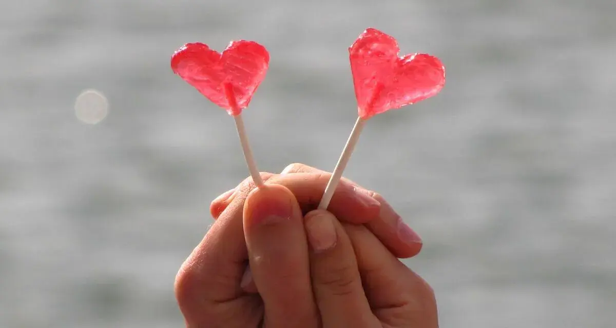 Dos piruletas rojas en forma de corazón, sostenidas por manos entrelazadas, como un símbolo de amor y una **venus carta astral**.