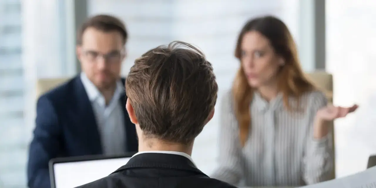 Besprechung mit einem Anwalt über Versicherungsansprüche. Eine Frau gestikuliert, während ein Mann mit Brille und ein Mann im Vordergrund zuhören.