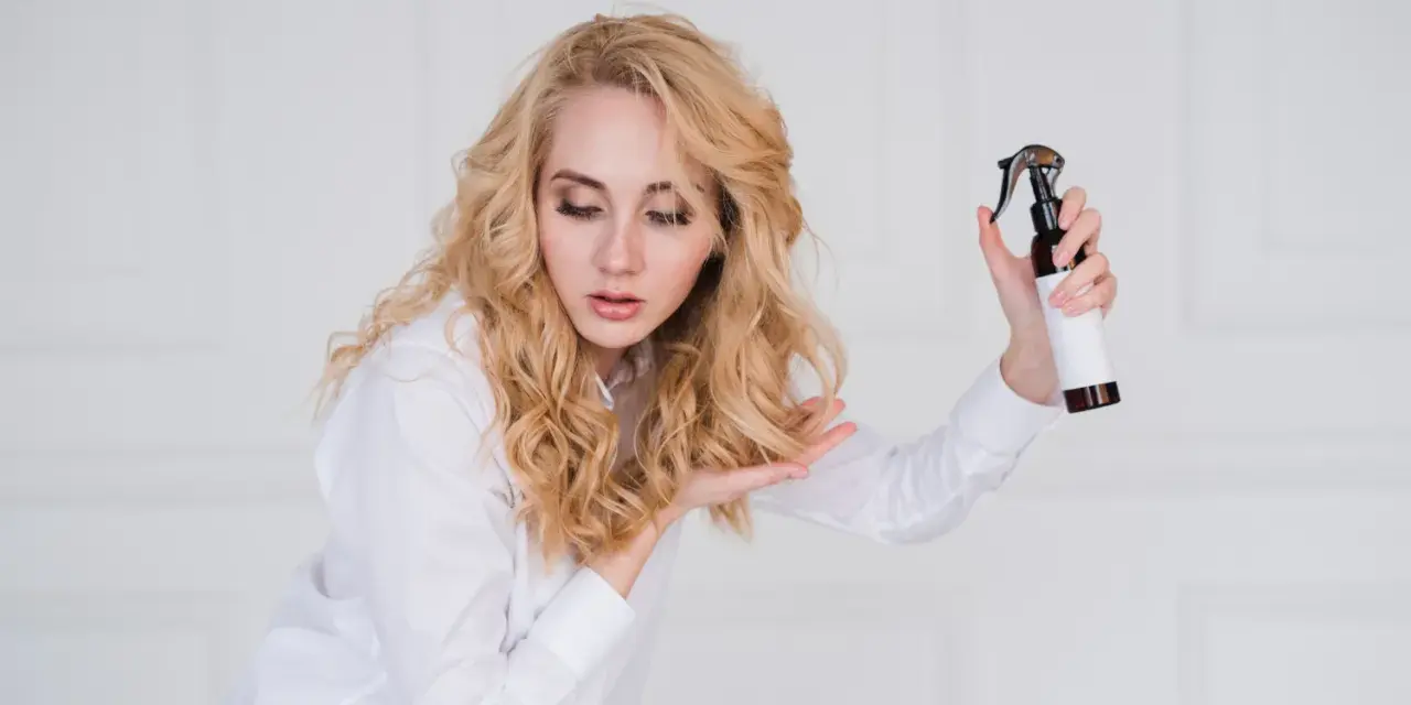 Blondynka z pięknymi, naturalnymi falami na włosach testuje nowy spray do stylizacji.