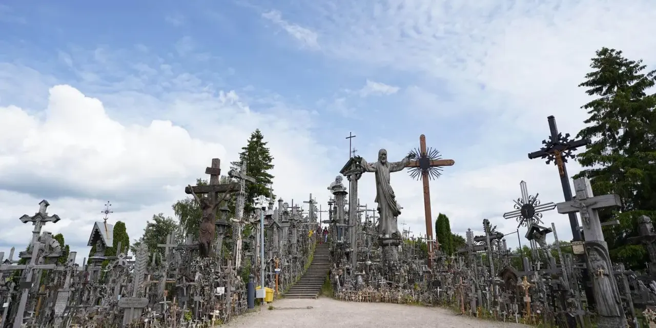 A vast mountain of crosses, with a statue of Jesus at its peak, stands under a cloudy sky.
