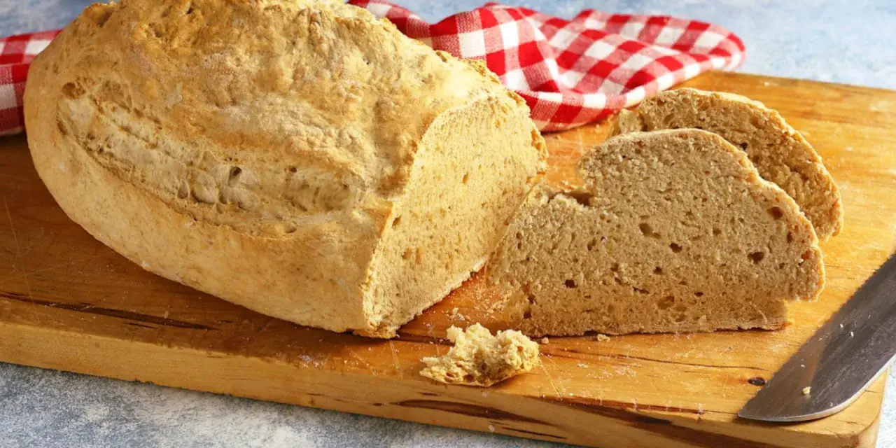 Pane casereccio con lievito istantaneo, tagliato su un tagliere di legno, con un tovagliolo a quadri rossi e bianchi.
