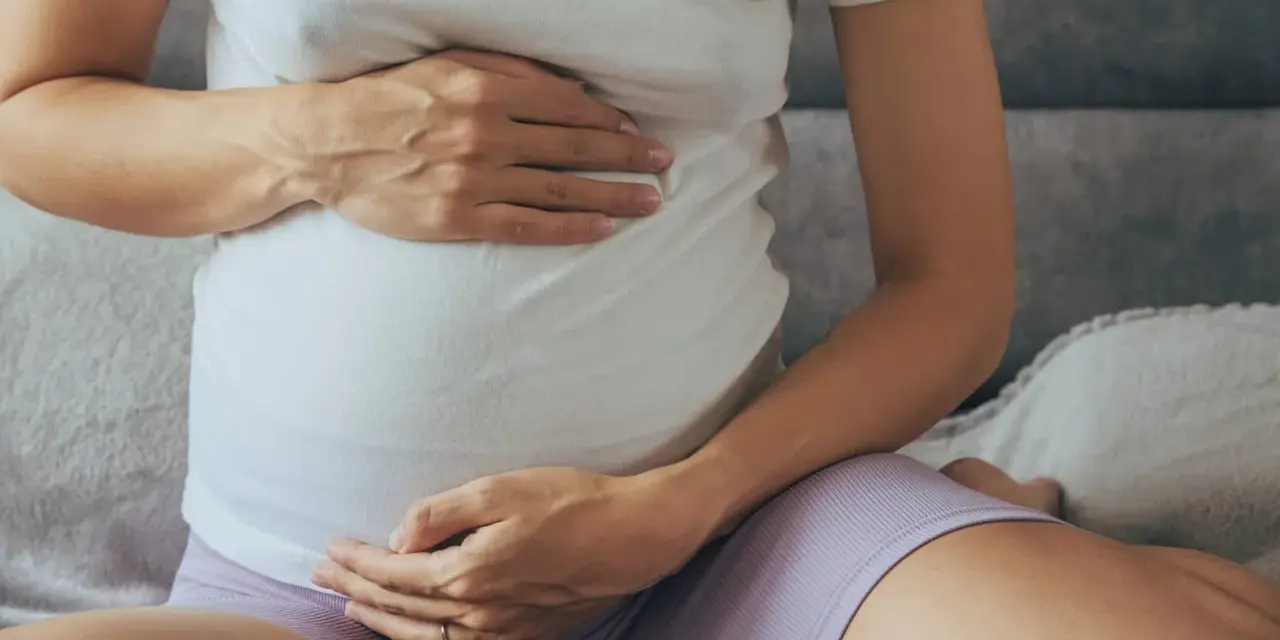 Brzuch kobiety w ciąży, z dłońmi delikatnie go obejmującymi.